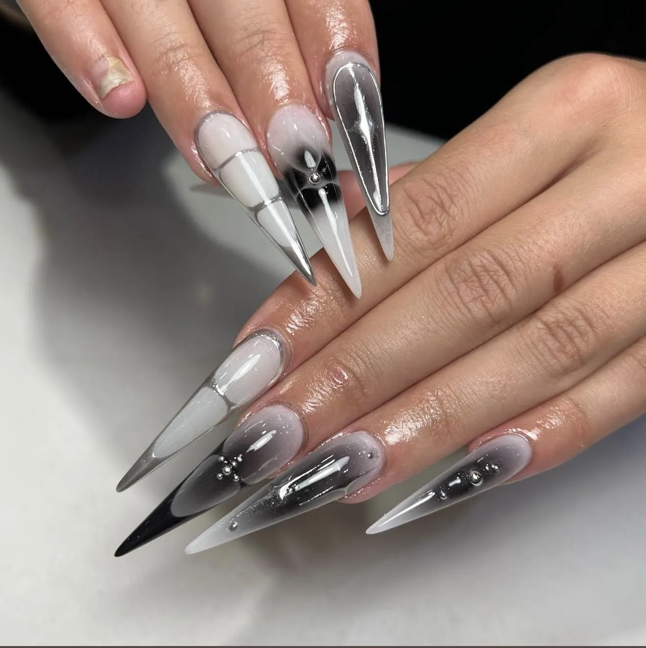 Long stiletto nails in smoky black and white with chrome accents and silver beads