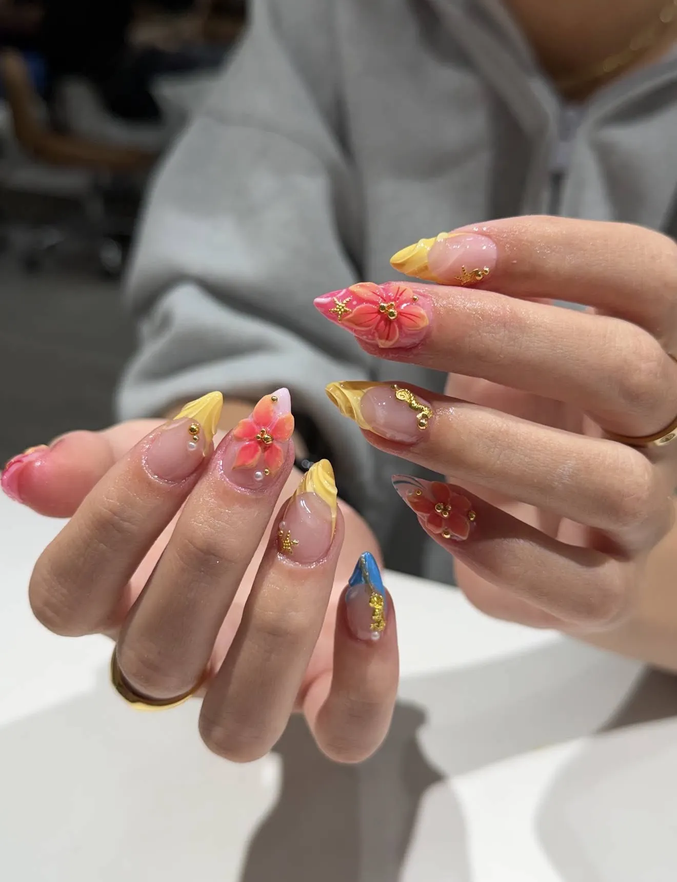 Almond nails with hand-painted pink hibiscus flowers, yellow tips and gold charms